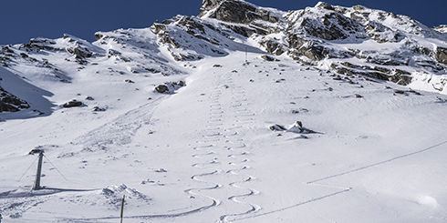 Pendio di montagna innevato con piste da sci a zig zag sotto un cielo azzurro e limpido.